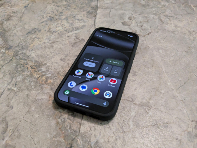 A picture of a black phone with the display on showing the Android home screen.