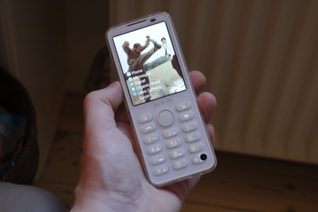 Picture of a white smartphone with small screen and built-in physical keyboard. Screen shows a shot from the movie Office Space (1999) where people are smashing a print machine out on a field.