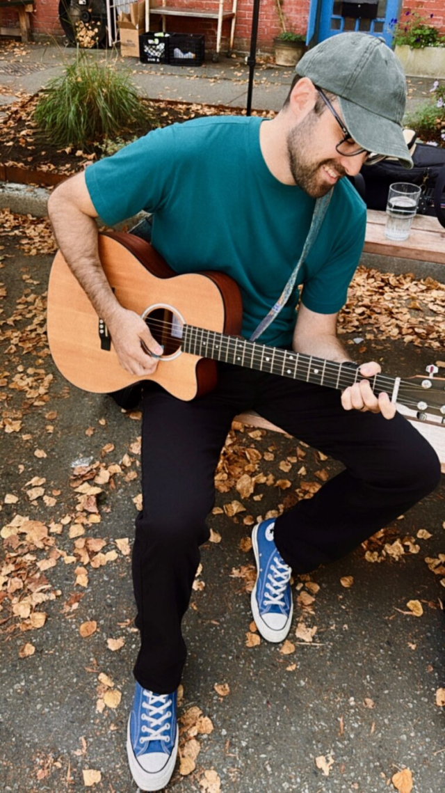 Picture of me sitting on a bench playing my acoustic guitar and smiling