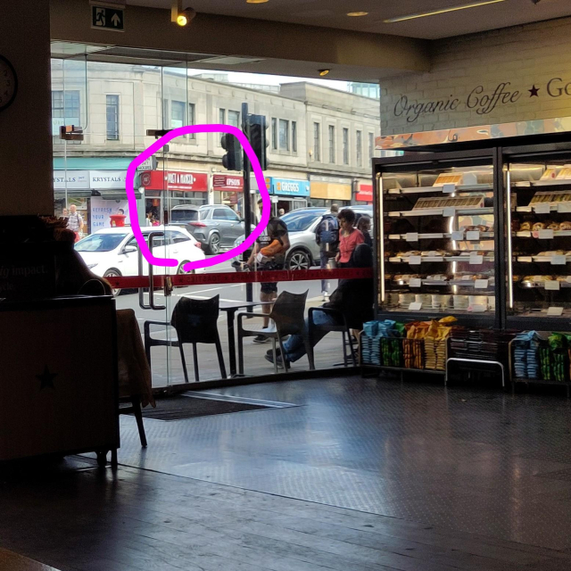 View from inside a Pret cafe with sandwich shelves etc. Through the window is a bust street, on the other side of which is a second branch of Pret.