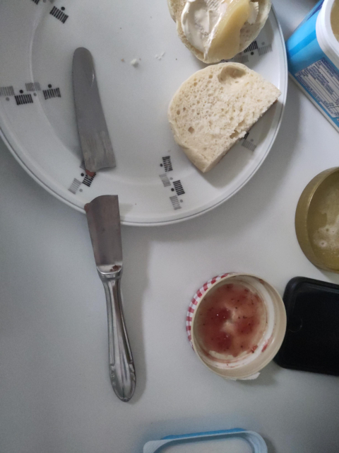 A plate with a sliced bread roll and broken knife. 