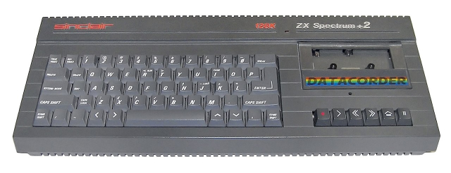 The Sinclair ZX Spectrum 2.  It's a black keyboard with a tape deck on its right side with the text 'datacorder' underneath on red, yellow, and blue lines.  Tape seek keys are presented below it. 