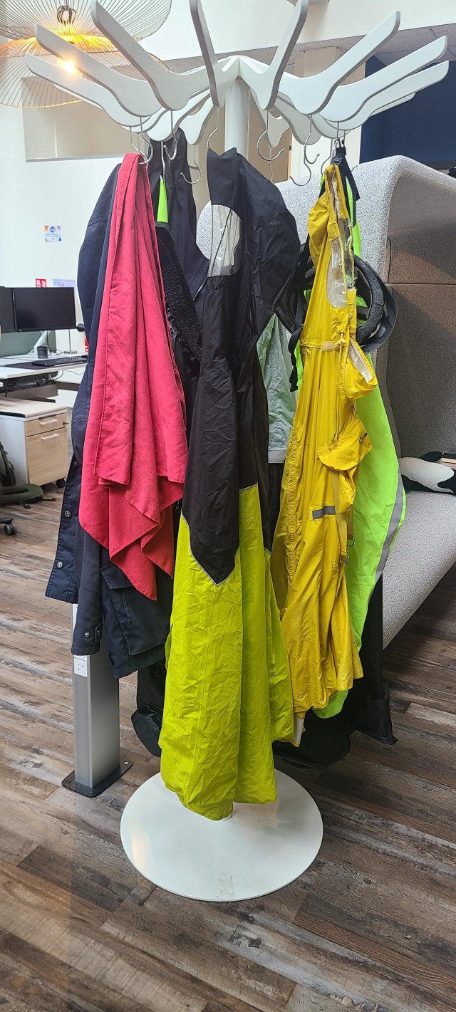 Photo prise au bureau, diverses capes de pluie et autres vestes imperméables sont accrochées à un porte-manteau.