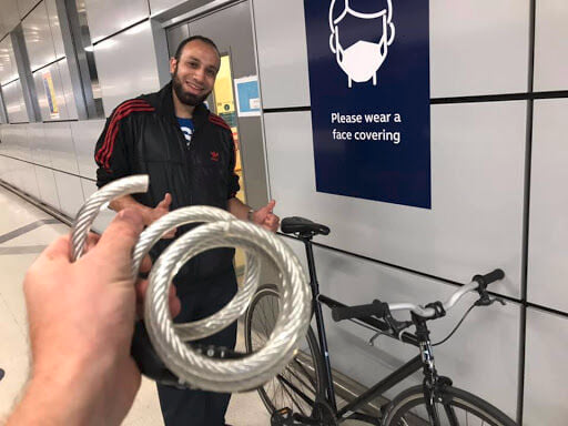 The picture is of a middle Eastern looking man smiling and holding a bike. In the foreground is a cut bike lock.
