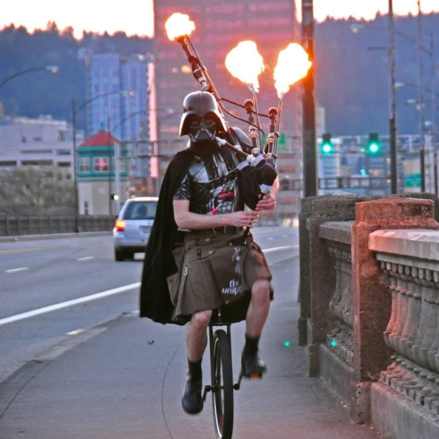 The famous unicycling Darth Vader on a bridge in Portland. He is playing flaming bagpipes. 