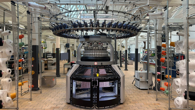 An enormous circular knitting machine several meters tall with dozens of bobbins around the central mechanism
