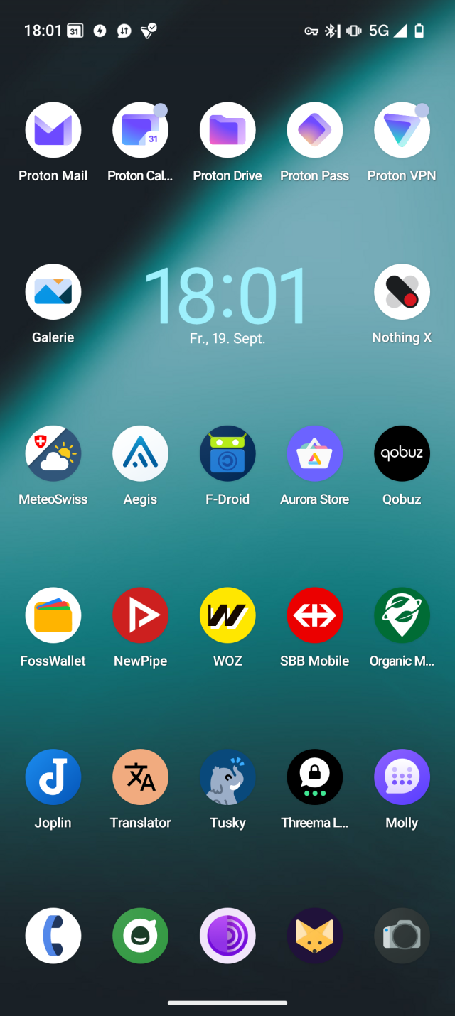 Screenshot des Homescreens eines Nothing Phone 2 mit LineageOS, auf dem überwiegend FLOSS-Apps (Free/Libre Open Source Software) zu sehen sind. Zu den abgebildeten Apps gehören: Proton (Mail, Kalender, Drive, Pass, VPN), Galerie (OS), Nothing X, Meteo Swiss, Aegis, F-Droid, Aurora Store, Qobuz, FossWallet, NewPipe, WoZ, SBB Mobile, Organic Maps, Joplin, Translate, Tusky, Threema Libre, Molly, Telefon (OS), Nachrichten (OS), Tor Browser, Fennec Browser und Kamera (OS).