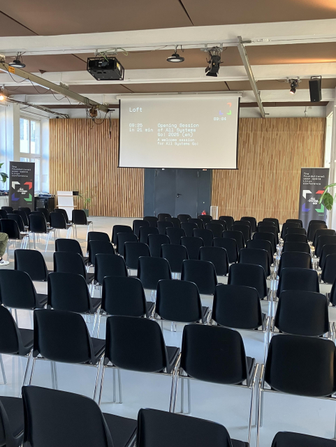 The main room for All Systems Go, slowly filling out; the overhead projector is showing the next talk, and counting down the minutes to the presentation’s time