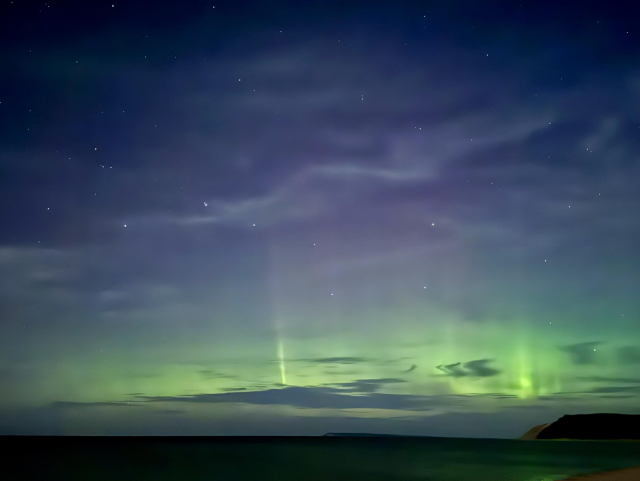 Green aurora borealis with columns blend with wispy clouds in a night sky over Lake Michigan