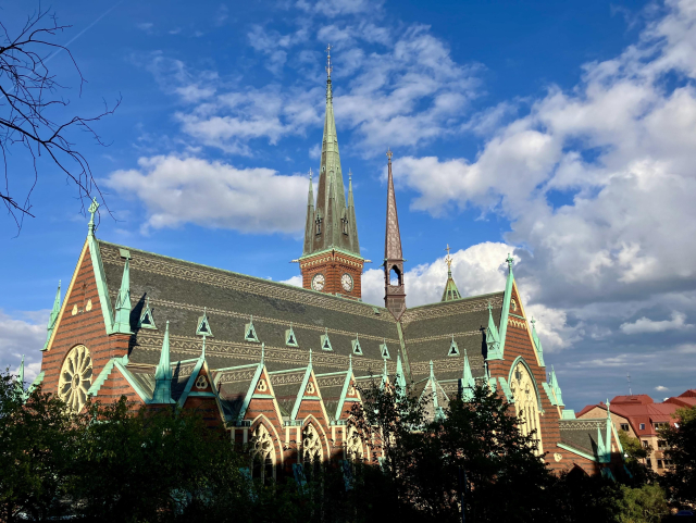 View of massive church with spires etc, with the bottom part in shade and blue sky above.