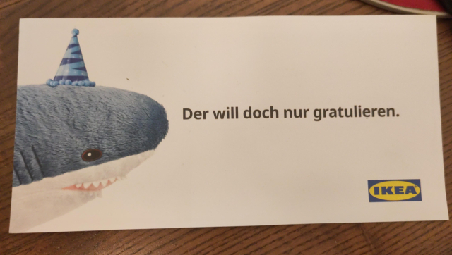 IKEA birthday card with a Blåhaj with a birthday hat. And "Der will doch nur gratulieren" (it only wants to congratualte) text.