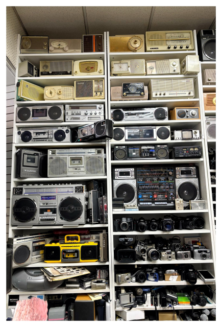 Photo of shelves at an electronics store — New Hi Tech Electronics on Canal Street in NYC — stacked to the ceiling with vintage radios, boomboxes, cameras, and other equipment.