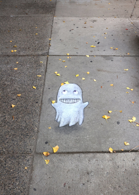 sidewalk chalk drawing of a ghost smiling up at yellow leaves that have fallen on her head