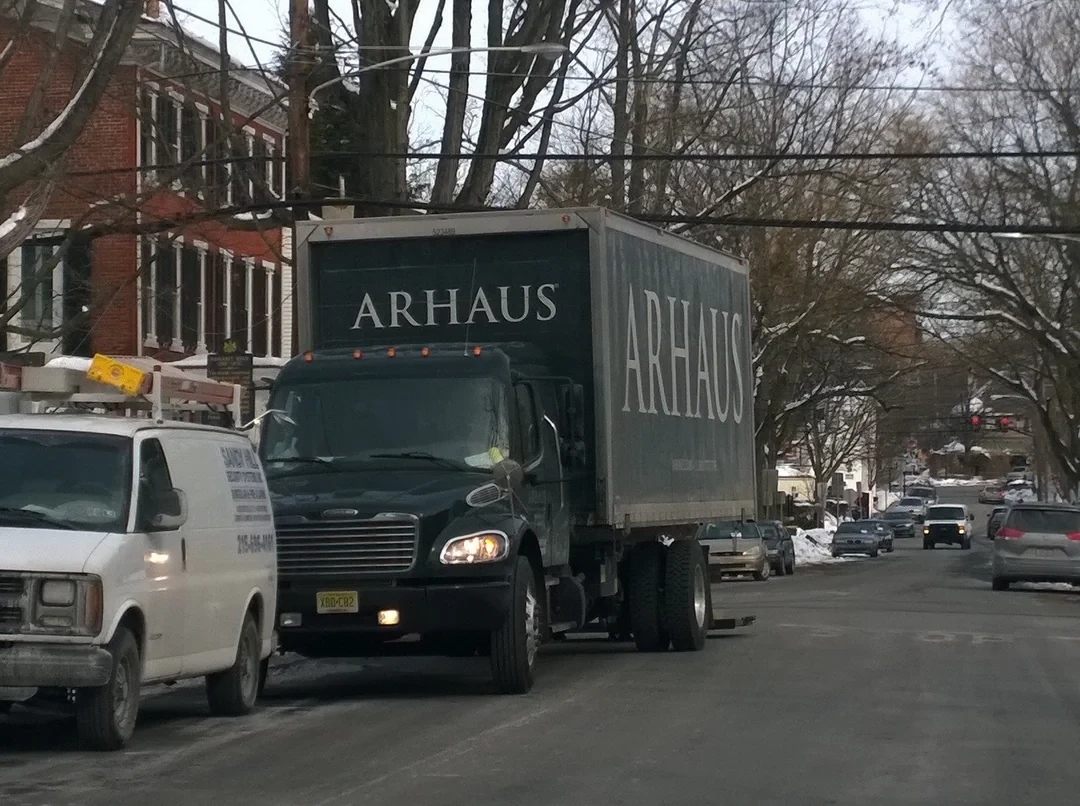 A black Arhaus furniture truck in the middle of a city street. 