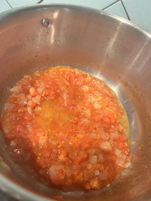 a steel pot with chopped onions and tomatoes slow cooking