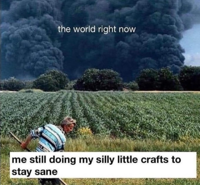 A meme about coping with global events. The image shows a person working in a green field, seemingly unconcerned with a massive plume of black smoke billowing in the background. The smoke is labeled "the world right now," and the person in the foreground is labeled "me still doing my silly little crafts to stay sane."