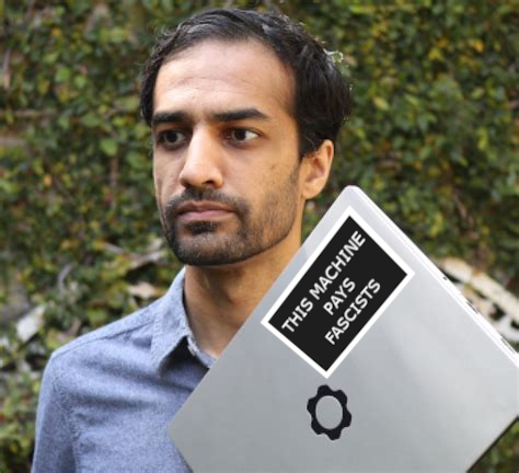 Framework CEO Nirav Patel holding a Framework laptop.  A sticker has been photoshopped onto the laptop reading "This machine pays Fascists".