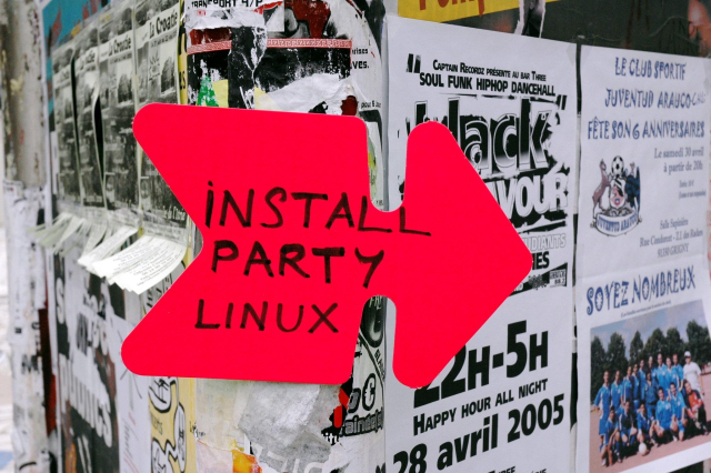A bright red arrow-shaped sign reads “Install Party Linux,” taped to a wall covered with overlapping event posters and flyers.