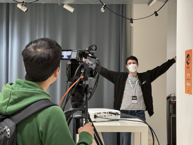 A photo of a volunteer operating a camera while another strikes a joyful pose