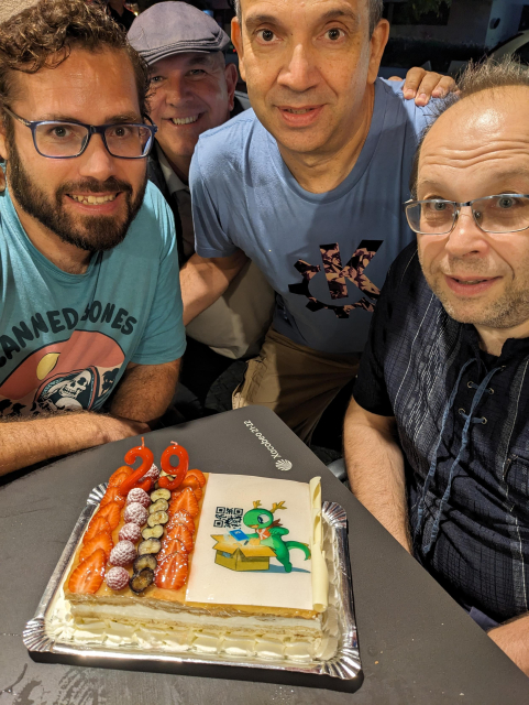 Smiling people around a cake decorated with Konqi