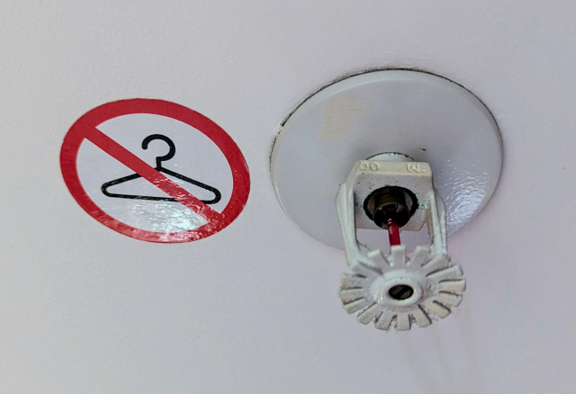 A picture of a fire sprinkler with a sticker showing crossed out clothes hanger.