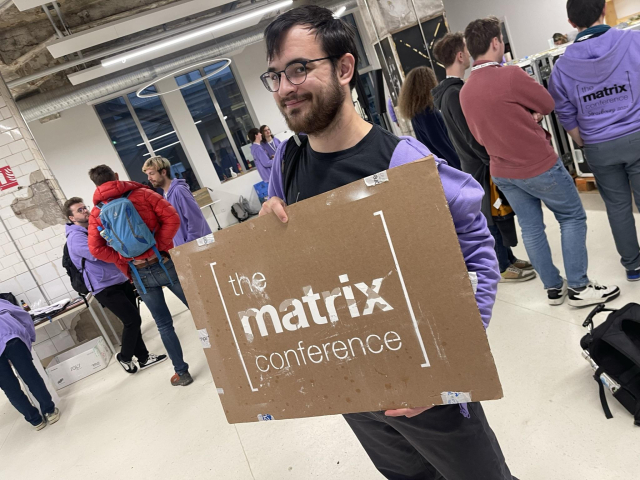 A picture of a man holding a piece of cardboard with the matrix conference logo chalk sprayed onto it