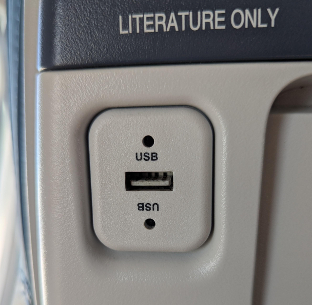 A USB Type-A receptacle in a seat of an aircraft.
The receptacle has the plastic part in the bottom which means it is mounted upside down. Above and below it is a label "USB," the bottom one upside down.