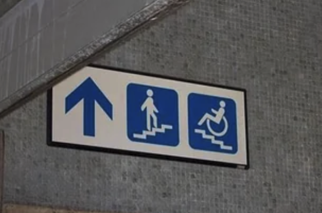 a sign with a arrow pointing up - with a drawing of a person walking up a flight of stairs, and next to that a person in a wheelchair going up a flight of stairs.