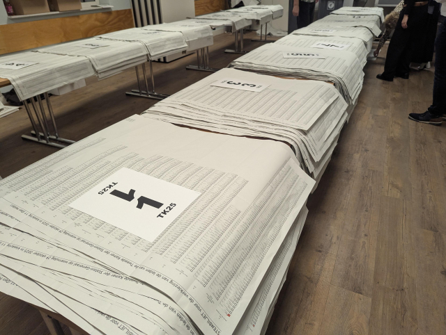 A view of desks full of unfolded ballots marked by party numbers.