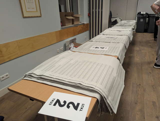 A view of desks full of unfolded ballots marked by party numbers