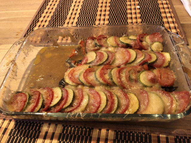 Un ratatouille, más bien tian de courgettes, en un refractario rectangular. Tiene filas de jitomates y calabacitas alternadas. Le faltan unos pedazos que ya están en sendas panzas.