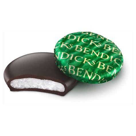 A photo of two Bendicks Bittermints on a white background. At the bottom is one unwrapped, and a bite taken out. You can see the mint fondant inside. Another wrapped mint sits over it, but slightly aside. Its green foil wrapper has the word "Bendicks" emblazoned many time over it.