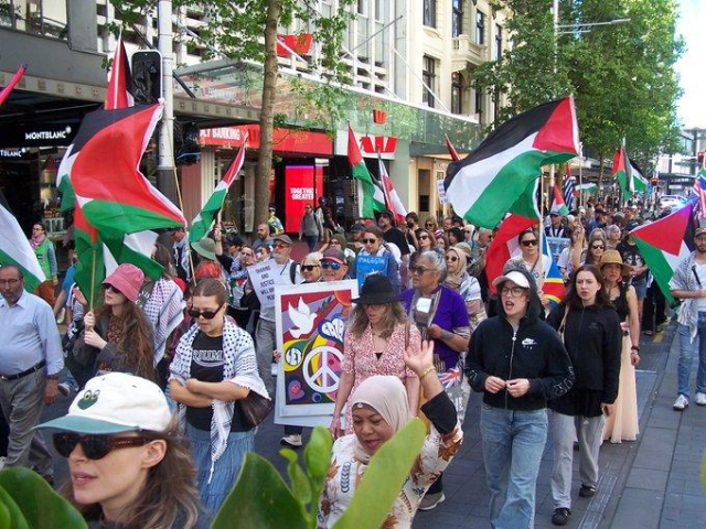 Large crowd marching through Auckland with flags and placards
