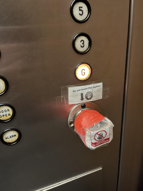 Photo of elevator buttons to select your destination. One button is covered by a bunch of red tape and padding that sticks out from the wall at least an inch. Written above it and on it are:
Do not touch this button
PLEASE DO NOT TOUCH