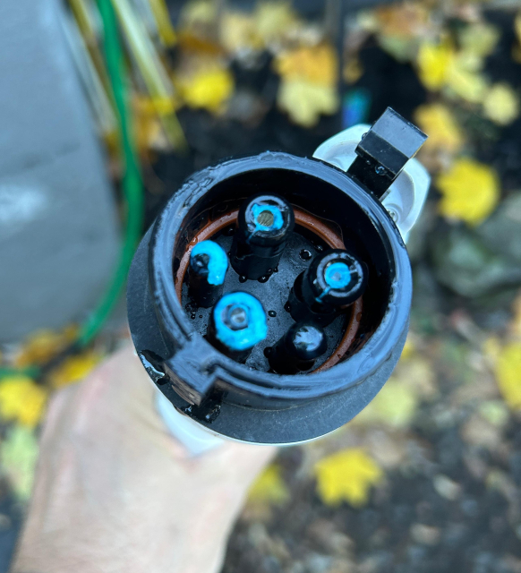 The top view of an EV charger plug being hand held. It shows there is water in it and the pins have a blue substance (it's corrosion)