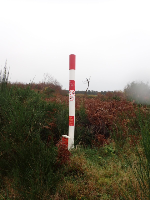 A red and white gas pipeline marker on a wet day.