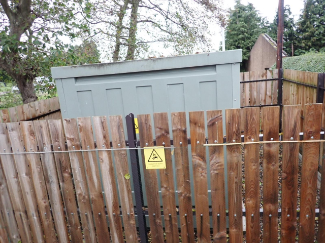 A grey utility cabinet enclosing an electricity substation. A wooden fence enlcoses the small compound 