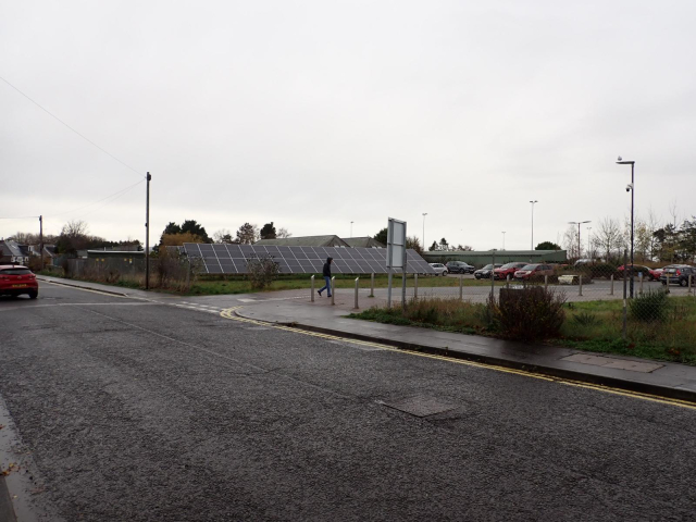 Ground-mounted solar panels adjacent to a car park off a residential road.