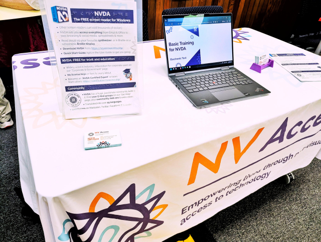 table with NV Access tablecloth, brochures, business cards and a laptop ready to demonstrate NVDA. Sascha and Quentin are hiding, nowhere to be seen in this image.
