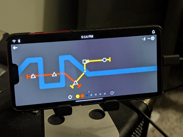 Photo of a phone on a stand running PostmarketOS playing Mini Metro.