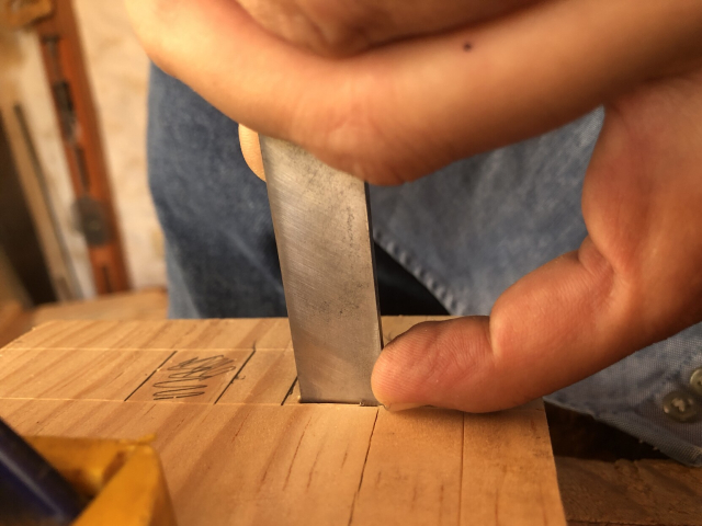 El formón vertical y hasta el fondo de una caja; mi dedo en un lado del formón con la uña bien pegada a la superficie de la madera.