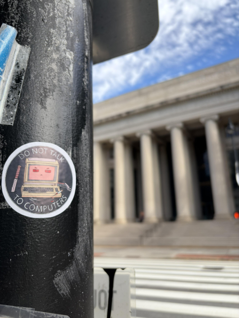 Sticker on a black pole that reads "Do not talk to computers" with a drawing of a retro computer, a knife, and a gun.