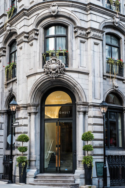 A corner stone building in a style that makes it look like it's European. The glass door making the rounded corner looks like reflecting a golden hue. There are three steps leading to it.