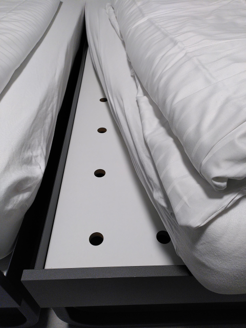 Die Matratze eines Hotelbetts ist zur Seite gezogen, darunter kommt statt eines Lattenrosts eine durchgehende MDF-Platte mit ein paar Luftlöchern zum Vorschein.