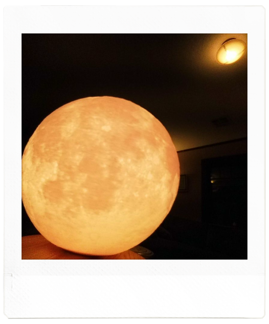 A golden blurry moon in close up, a dark room behind and a light fixture on the ceiling that hopefully looks teensy bit like a glowing UFO