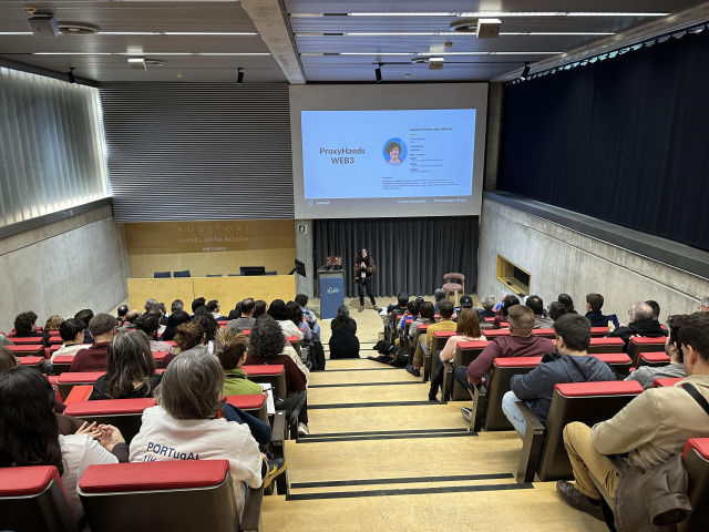 Carmen Torrecillas en el escenario del auditorio de la a11yConf 2025 en Gerona hablando de visualizacion de datos accesible delante de la audiencia, en un plan más amplio con la sala llena de asistentes