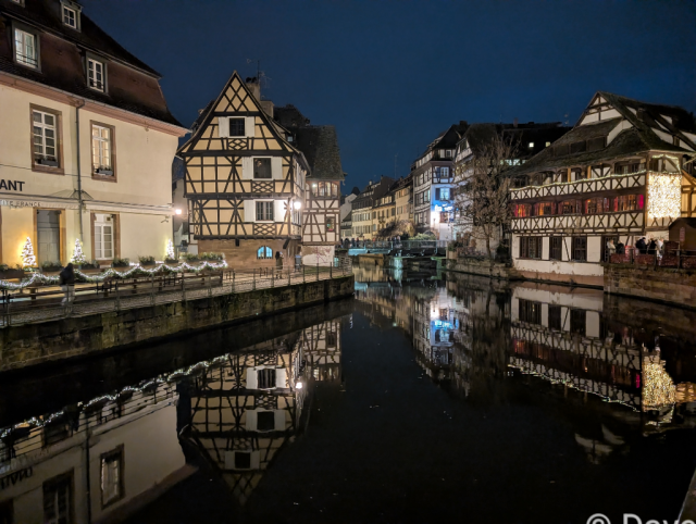 Illuminated medieval buildings reflected in a still, dark river.