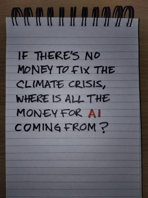 A spiral bound lined notepad showing the handwritten message: "IF THERE'S NO MONEY TO FIX THE CLIMATE CRISIS, WHERE IS ALL THE MONEY FOR AI COMING FROM?". Text is written in all caps, in black marker apart from AI which is in red.