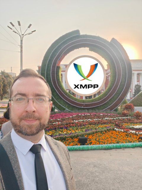 Selfie with the XMPP logo placed against a large circular hedge sculpture in a park in Dushanbe.
