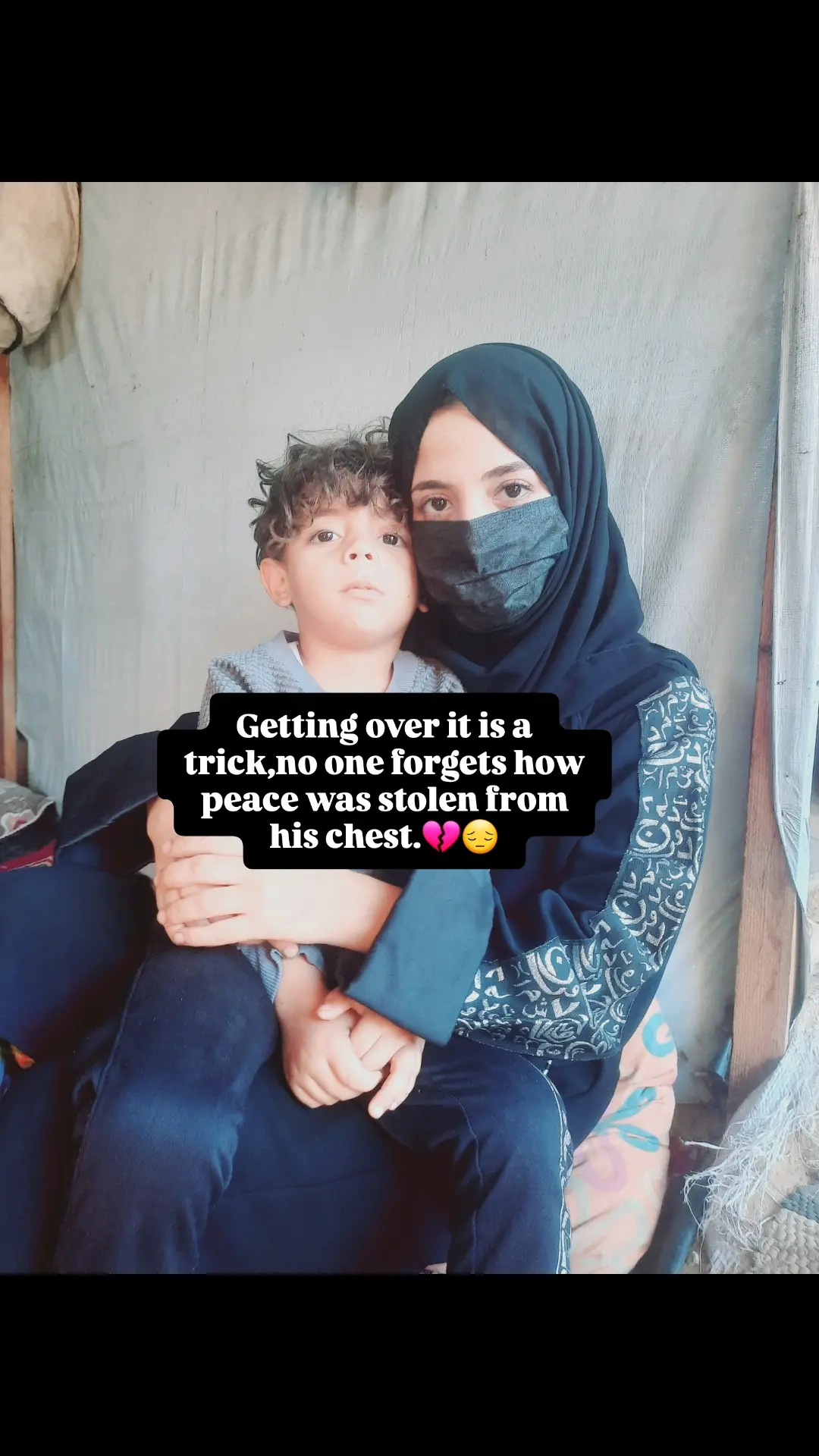 Baraa, a 28-year-old woman, wearing a medical mask, is holding her four-and-a-half-year-old son, Ibrahim, as they look directly at the camera.